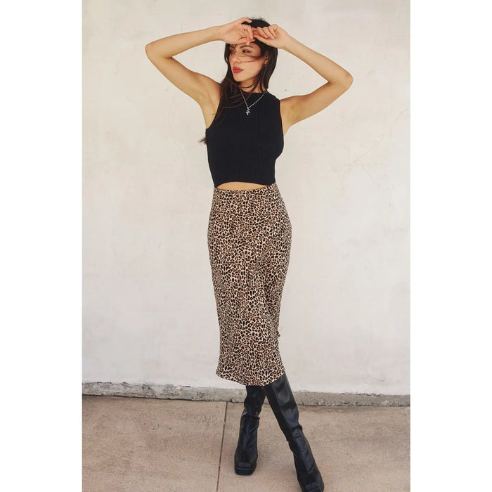 Person wearing a black sleeveless top and leopard print skirt against a white wall.