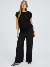 Woman wearing a black textured top and wide-leg pants on a white background