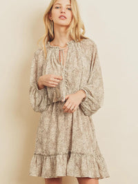 Woman wearing a tan floral dress against a plain background