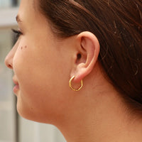 Woman wearing small 18K gold geometric huggie hoop earrings from Cashato – minimalist, waterproof, and tarnish-resistant jewelry.