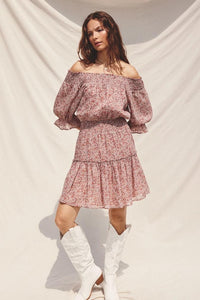 Woman wearing a floral off-shoulder dress with white knee-high boots against a plain background