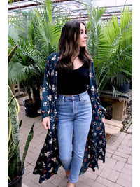 Woman wearing a floral kimono over a black top and blue jeans in a garden setting.
