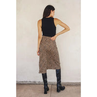 Woman wearing a black sleeveless top and leopard print skirt with black knee-high boots against a plain wall.