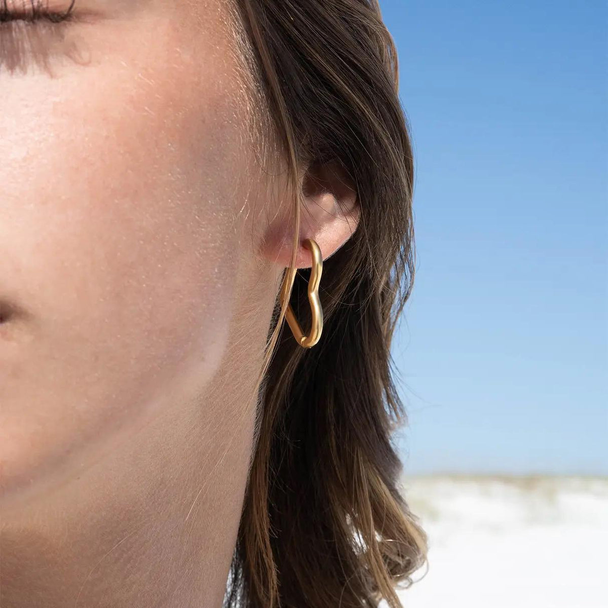 Close-up of a person wearing large gold hoop earring with a blurred beach background