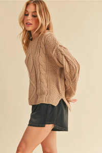 Woman wearing a beige cable knit sweater and black shorts on a beige background