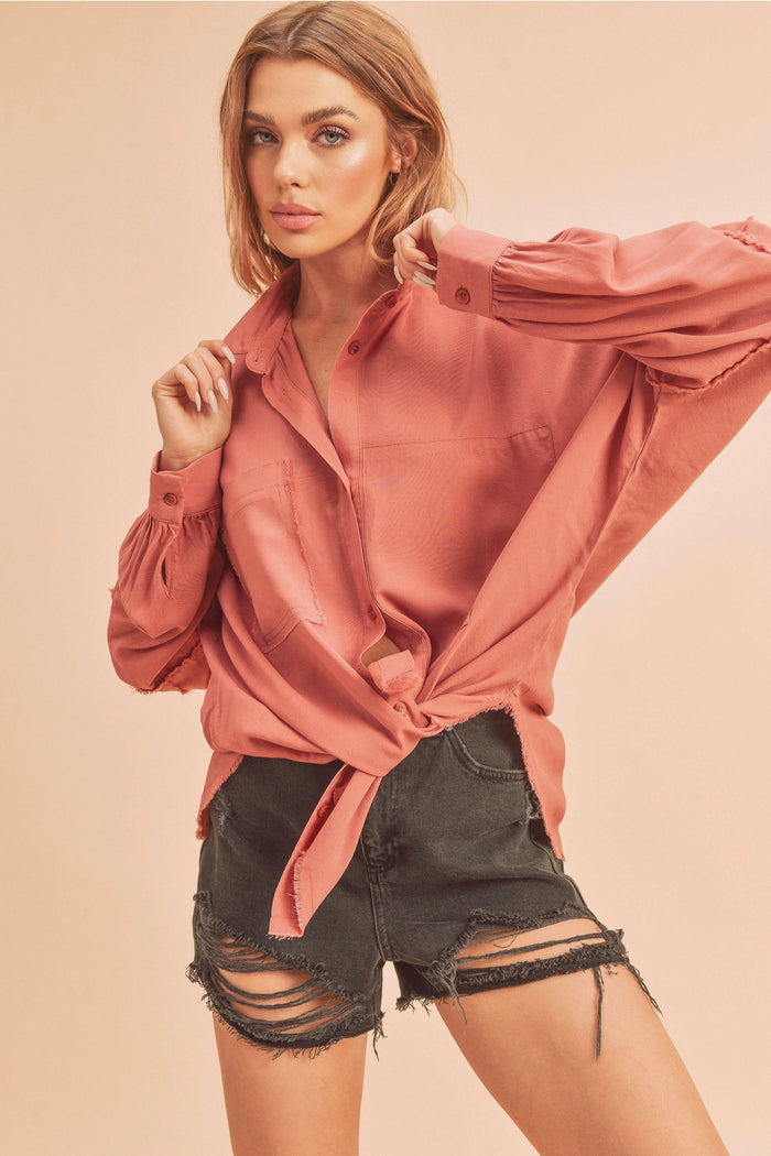Woman wearing a pink blouse and black shorts against a beige background