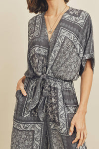 Person wearing a gray patterned jumpsuit on a beige background