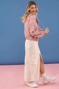 Woman wearing a pink jacket and white skirt against a blue and pink background