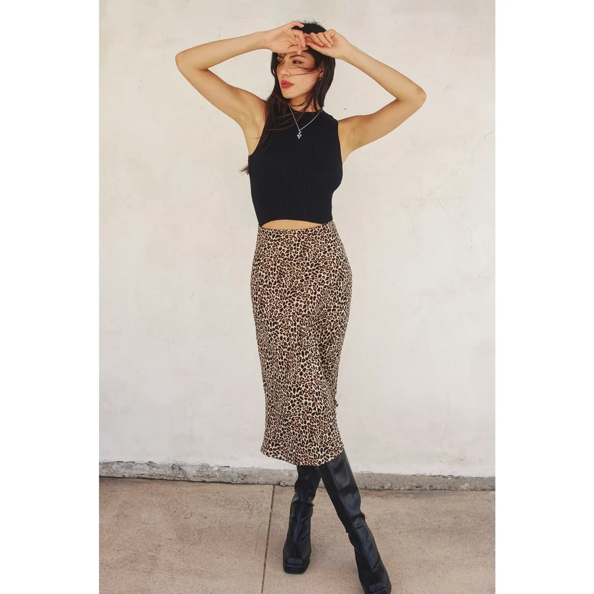 Person wearing a black sleeveless top and leopard print skirt against a white wall.