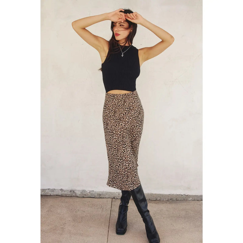 Person wearing a black sleeveless top and leopard print skirt against a white wall.