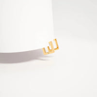 Gold square earring hoop on a gray belt against a white background