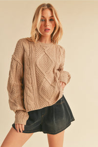 Woman wearing a beige cable knit sweater and black shorts on a beige background