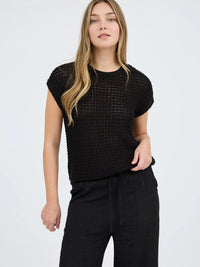 Woman wearing a black textured sleeveless top and black pants on a white background