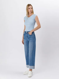 Woman wearing a light blue sleeveless top and jeans on a white background