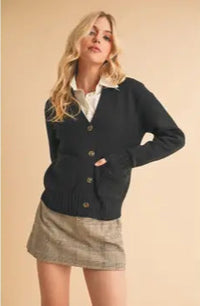 Woman wearing a navy cardigan over a white shirt and plaid skirt on a beige background