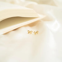Gold bow-shaped earrings on a soft beige fabric background