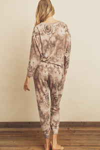 Person wearing a patterned outfit standing against a plain wall.