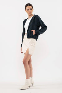 Woman wearing a navy cardigan, white top, and shorts with white boots on a white background