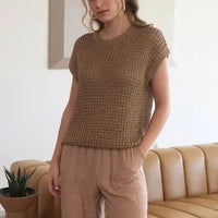 Woman wearing a brown knitted top and beige pants in a living room setting.