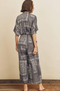 Woman wearing a patterned jumpsuit standing against a plain wall.