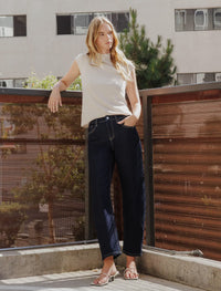 Model wearing high rise dark wash slim barrel jeans standing on a rooftop.