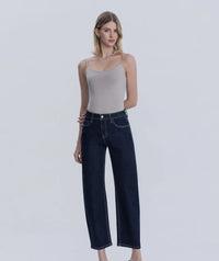 Woman wearing a beige top and dark blue jeans on a white background