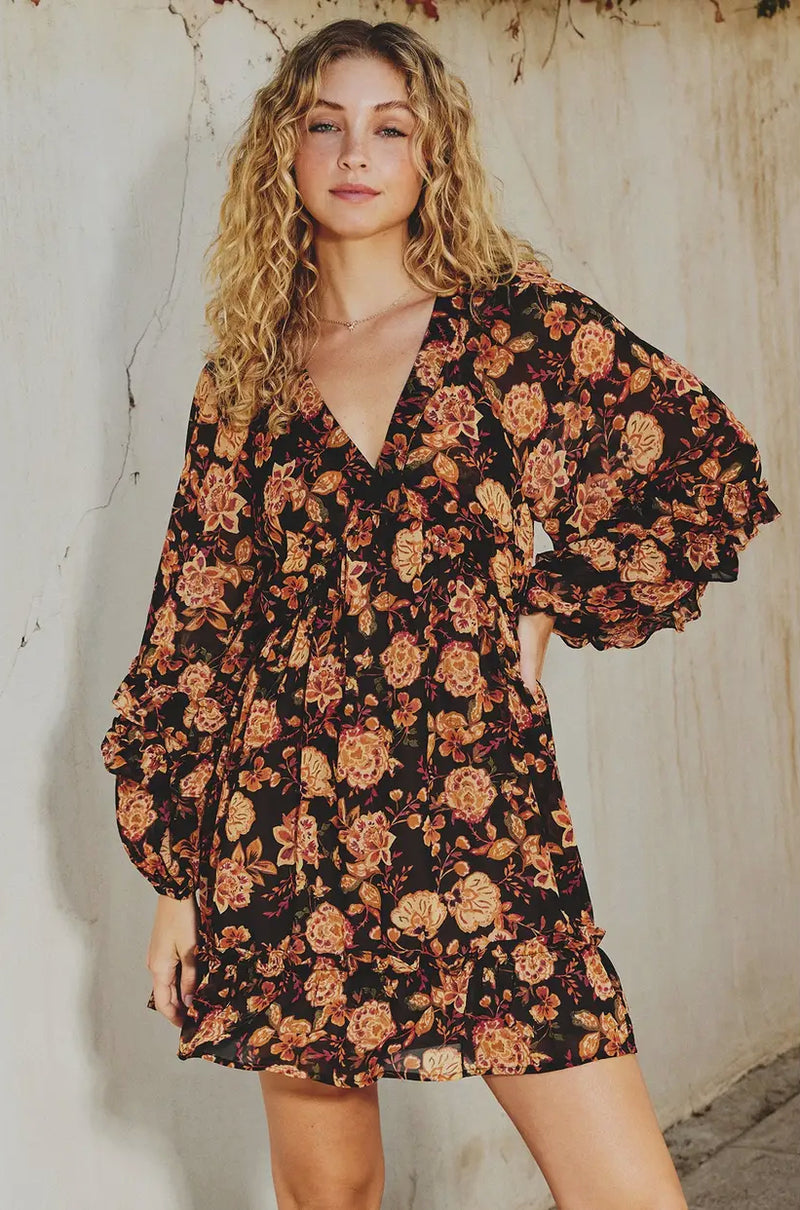 Woman wearing a floral dress against a textured wall.