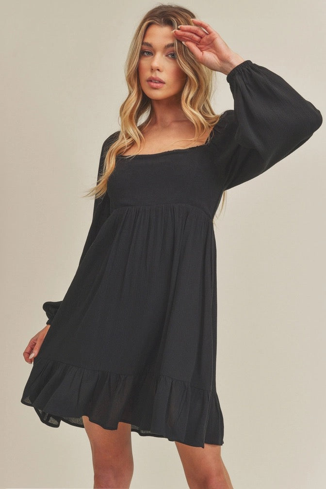 Woman wearing a black dress with long sleeves on a plain background