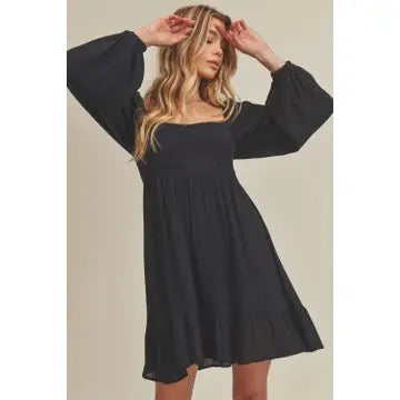 Woman wearing a black dress with wide sleeves against a beige background