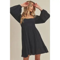 Woman wearing a black dress with wide sleeves against a beige background