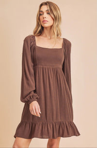 Woman wearing a brown dress with long sleeves against a beige background