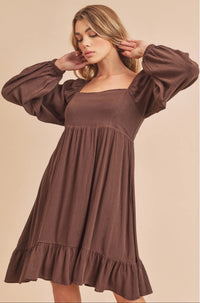 Woman wearing a brown dress with long sleeves on a beige background