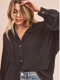 Woman wearing a black oversized shirt and blue jeans against a pink background