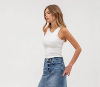 Woman wearing a white top and blue denim skirt on a plain background