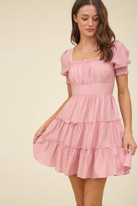 Woman wearing a pink dress with ruffled sleeves and tiered skirt on a beige background