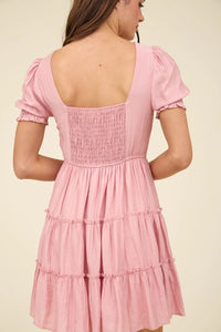 Pink dress with smocked bodice and tiered skirt on a plain background