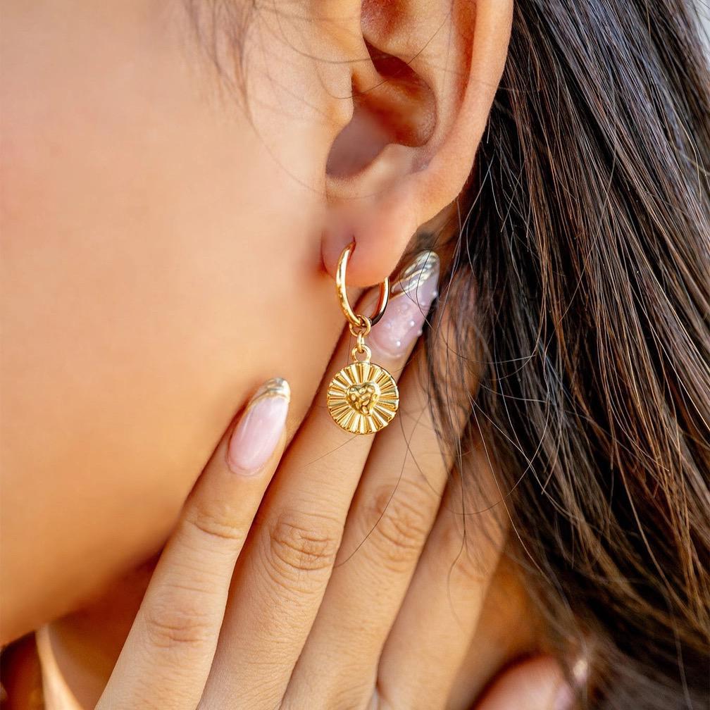Close-up of a person wearing a gold hoop earring with a sunflower charm.