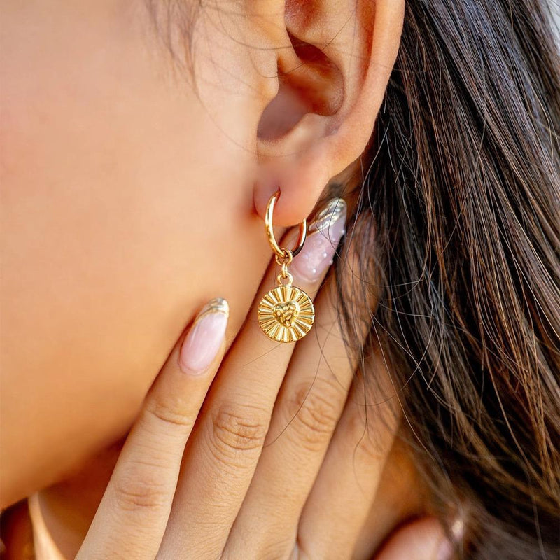 Close-up of a person wearing a gold hoop earring with a sunflower charm.