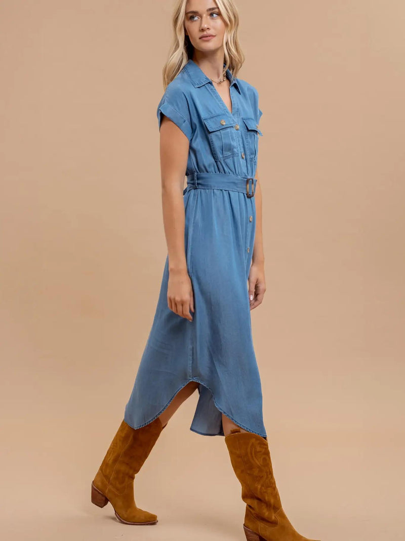 Woman wearing a blue denim dress with brown knee-high boots on a beige background