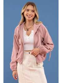 Woman wearing a pink jacket over a white top and light-colored pants on a blue background