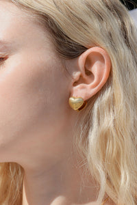 Cashato heart-shaped gold huggie earring with ribbed texture worn on ear