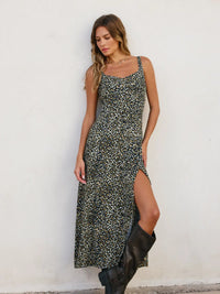 Woman wearing a leopard print dress with a slit, standing against a white wall.