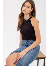Woman wearing a black sleeveless top and blue denim skirt sitting on a white background